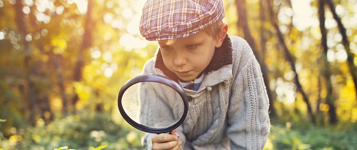 Kind im Wald mit einer Lupe in der Hand