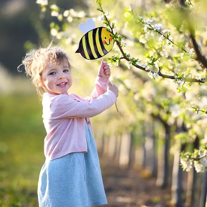 Kita-Projekt zum Thema Bienen: Mädchen mit gebastelter Biene am Baum