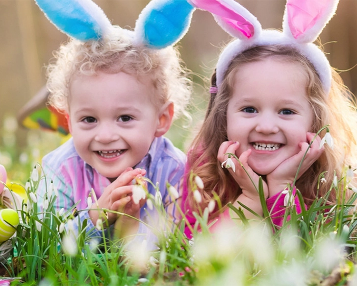 Ostern mit Kindern Zwei Mädchen mit Hasenohren liegen im Feld neben Ostereier
