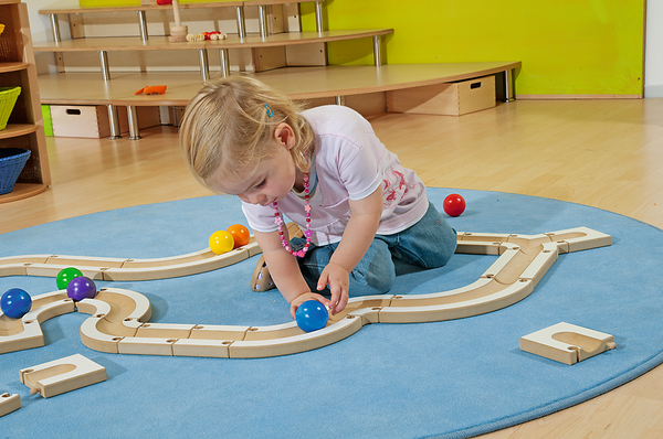 child playing, wooden train set, colorful balls, indoor playground, blue rug