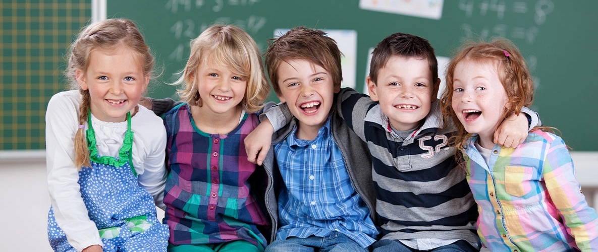 Kinder sitzen in einer Reihe vor einer Schultafel