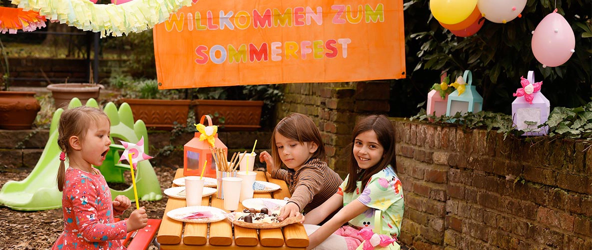 Kinder sitzen am Tisch beim Sommerfest