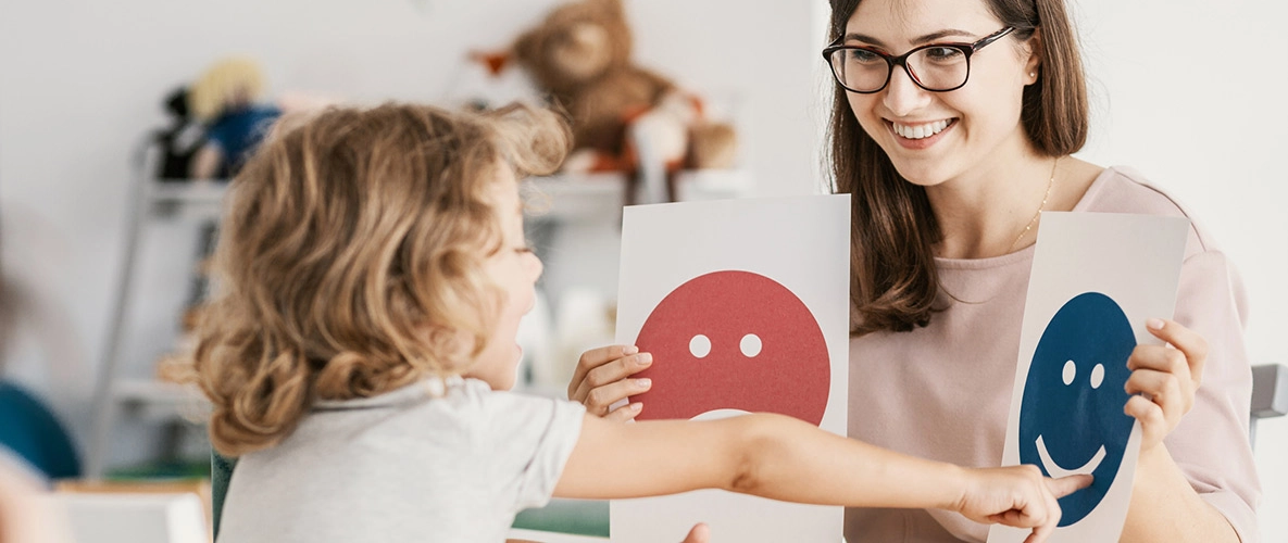 Emotionale Entwicklung bei Kindern Frau zeigt Kind ein lachenden und traurigen Smiley